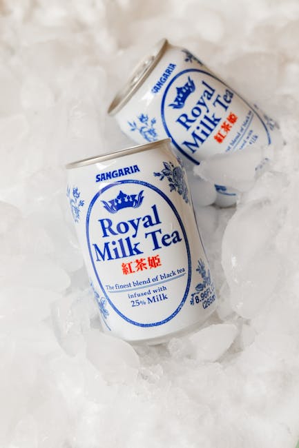 Two cans of Sangaria Royal Milk Tea with blue and white labels are partially submerged in crushed ice outdoors, likely on a pavement or sidewalk during daylight. The cans are positioned at slight angles, with one tilted towards the viewer and the other behind it. The background appears to be a neutral surface, emphasizing the cold packaging and beverage cans. This image may relate to the process of transporting or packing beverages during a home relocation, illustrating careful handling and packaging of miscellaneous items, relevant to removals services offered by Man with Van Canning Town.