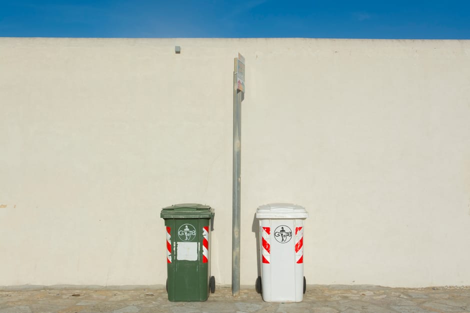 A black wheelie bin labeled 'St. John's' positioned on the sidewalk at night, filled with various waste items including cardboard boxes, plastic packaging, and paper, with the lid slightly open. The b